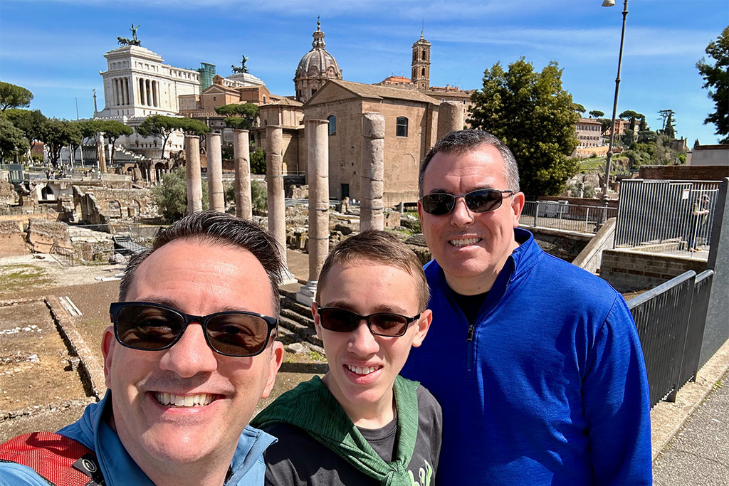 Photo of family with two dads and one child in front on ancient ruins