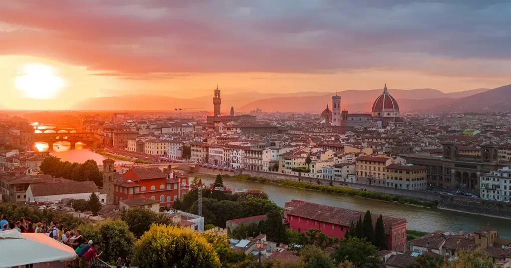 A golden sunset illuminates the Florence skyline, highlighting the Duomo and Ponte Vecchio over the Arno River. Florence is a great option for art lovers' first time in Italy.