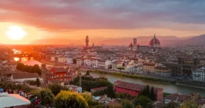A golden sunset illuminates the Florence skyline, highlighting the Duomo and Ponte Vecchio over the Arno River. Florence is a great option for art lovers' first time in Italy.