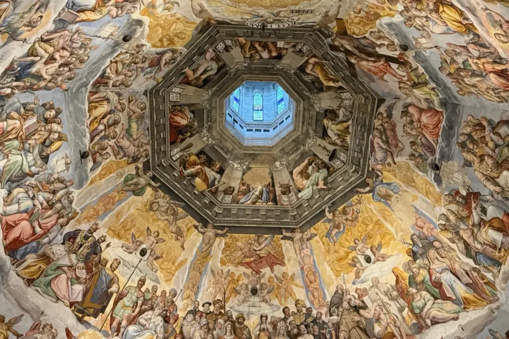 Looking up into the ornate, octagonal dome of the Florence Cathedral, featuring Giorgio Vasari's massive fresco "The Last Judgment" under a lantern.