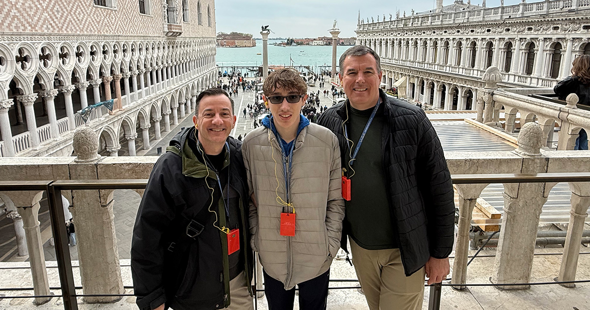 In this Italy trip with teenagers, a family of three smiles for a photo on a St. Mark's Square balcony in Venice.