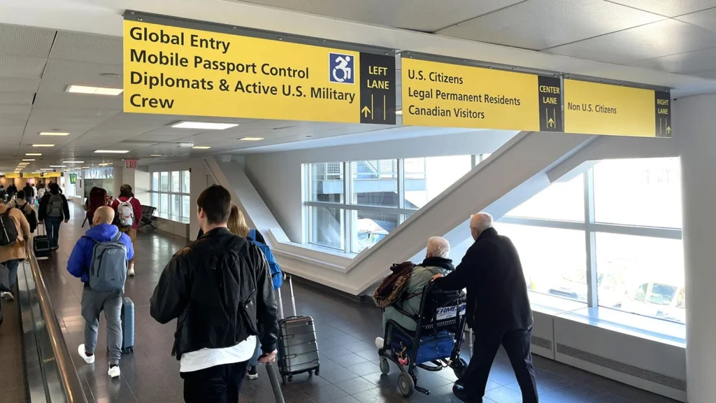Travelers walk down an airport corridor beneath large yellow signs directing people to Global Entry, U.S. Citizens, and Non U.S. Citizens lanes.