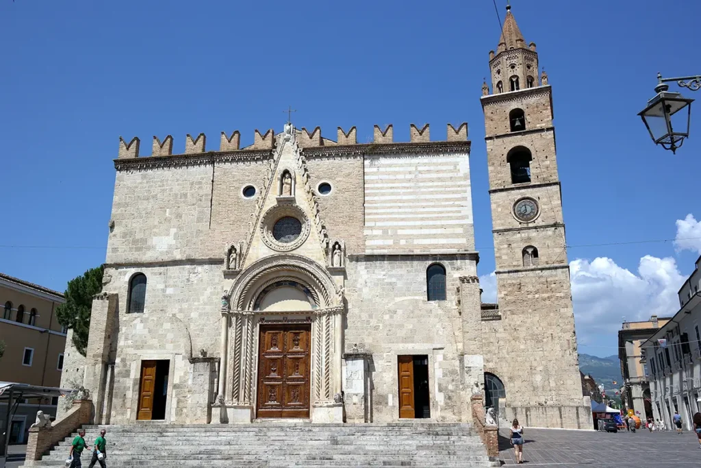The ancient stone facade and decorative bell tower of the Cathedral of Teramo stand in a sunlit public square.