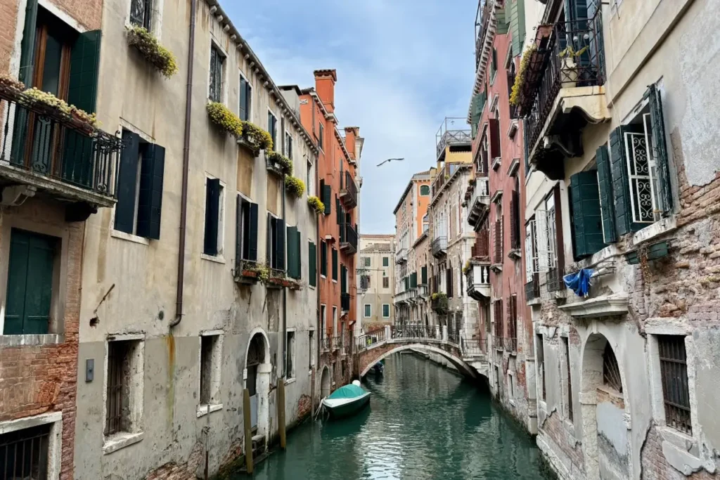 A quiet Venetian canal with a small arched bridge, a covered boat, and historic shuttered buildings.